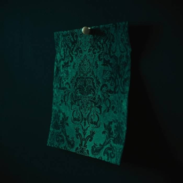 Victorian green wallpaper sample pinned to a dark wall